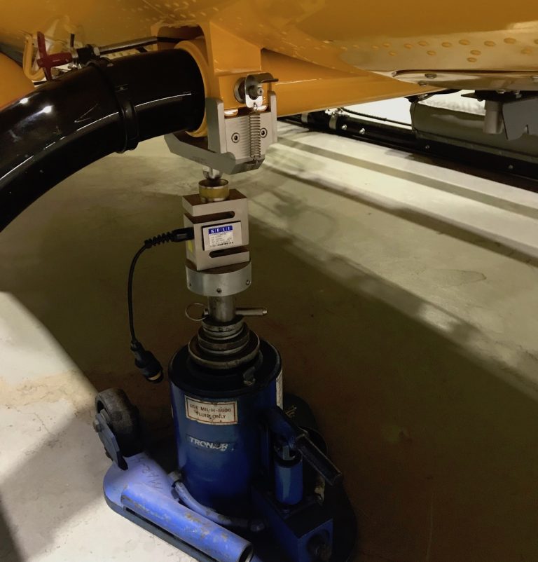 Close up of a helicopter weighing jack placed underneath the right front skid of a yellow helicopter.